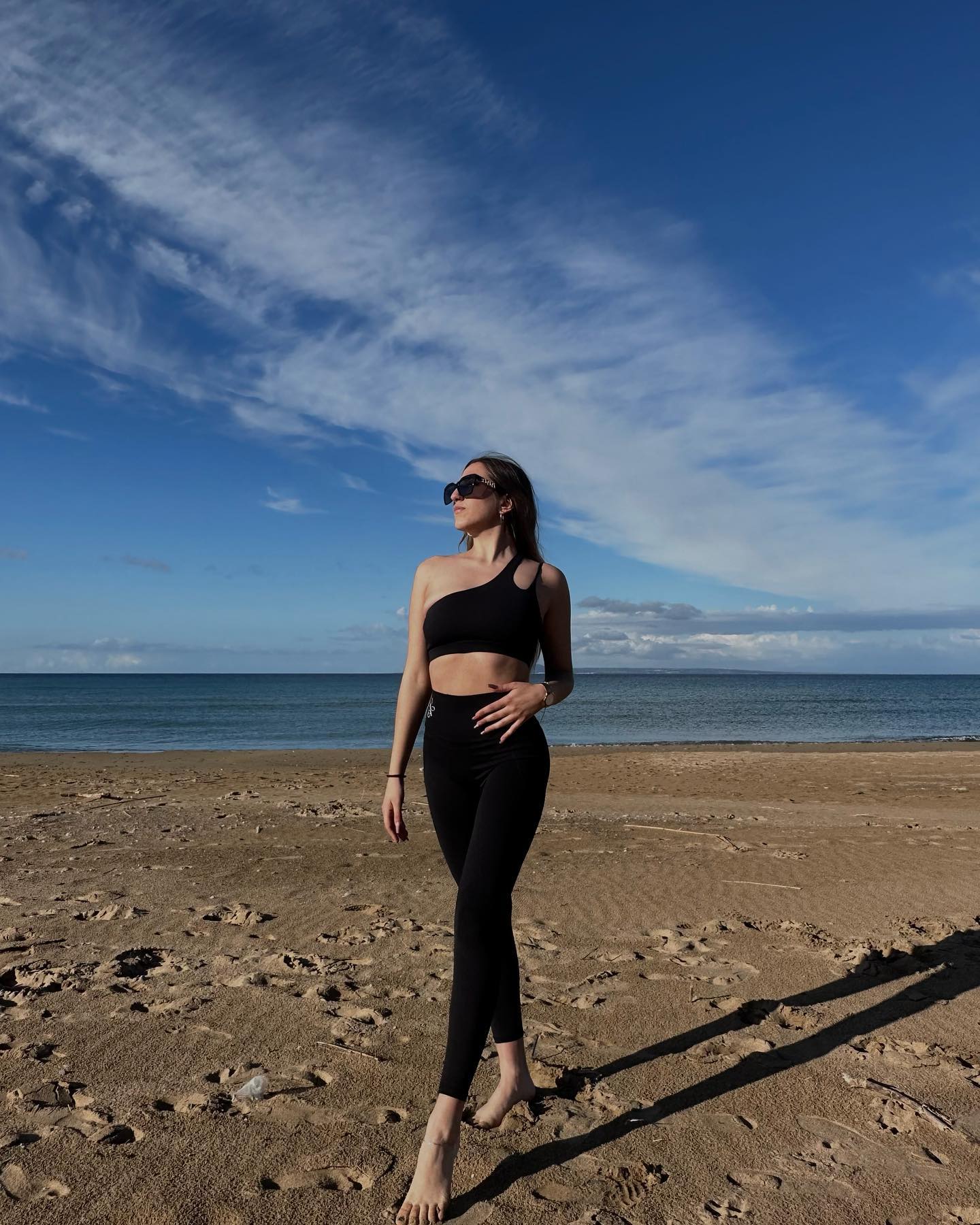 Brunette Model Radiating Confidence in Black One-Shoulder Sports Bra on Greek Beach